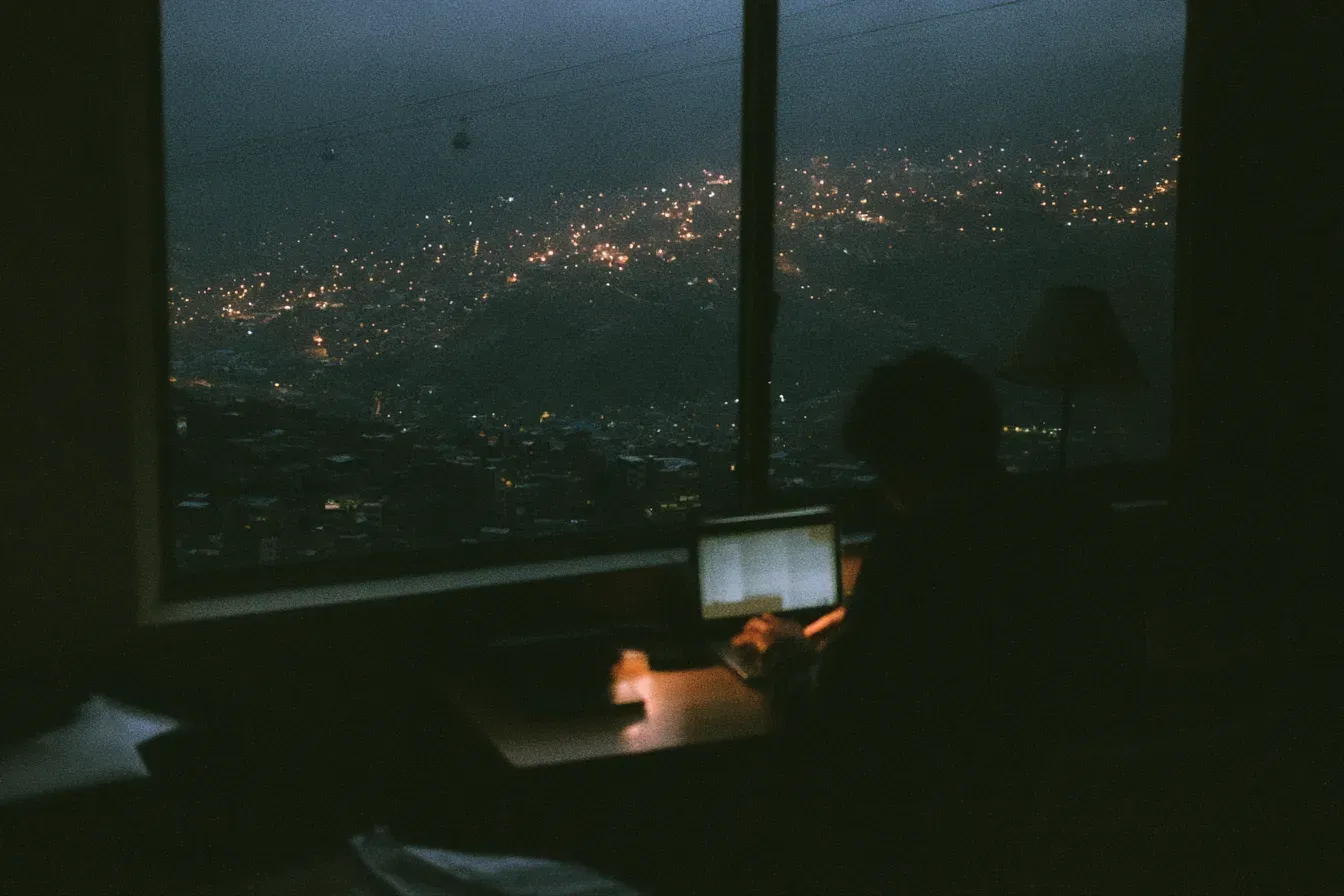A freelancer working at a desk by a window overlooking La Paz at dusk